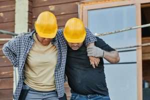 Two construction workers in hard hats assisting each other at a building site, highlighting teamwork.